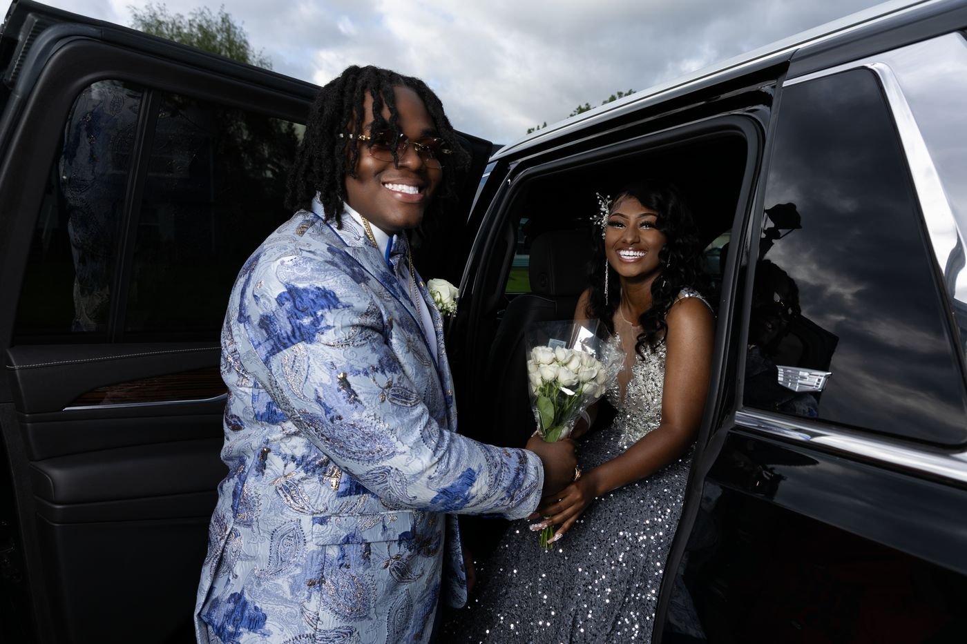Couple in formal wear posing at the open door of a black SUV