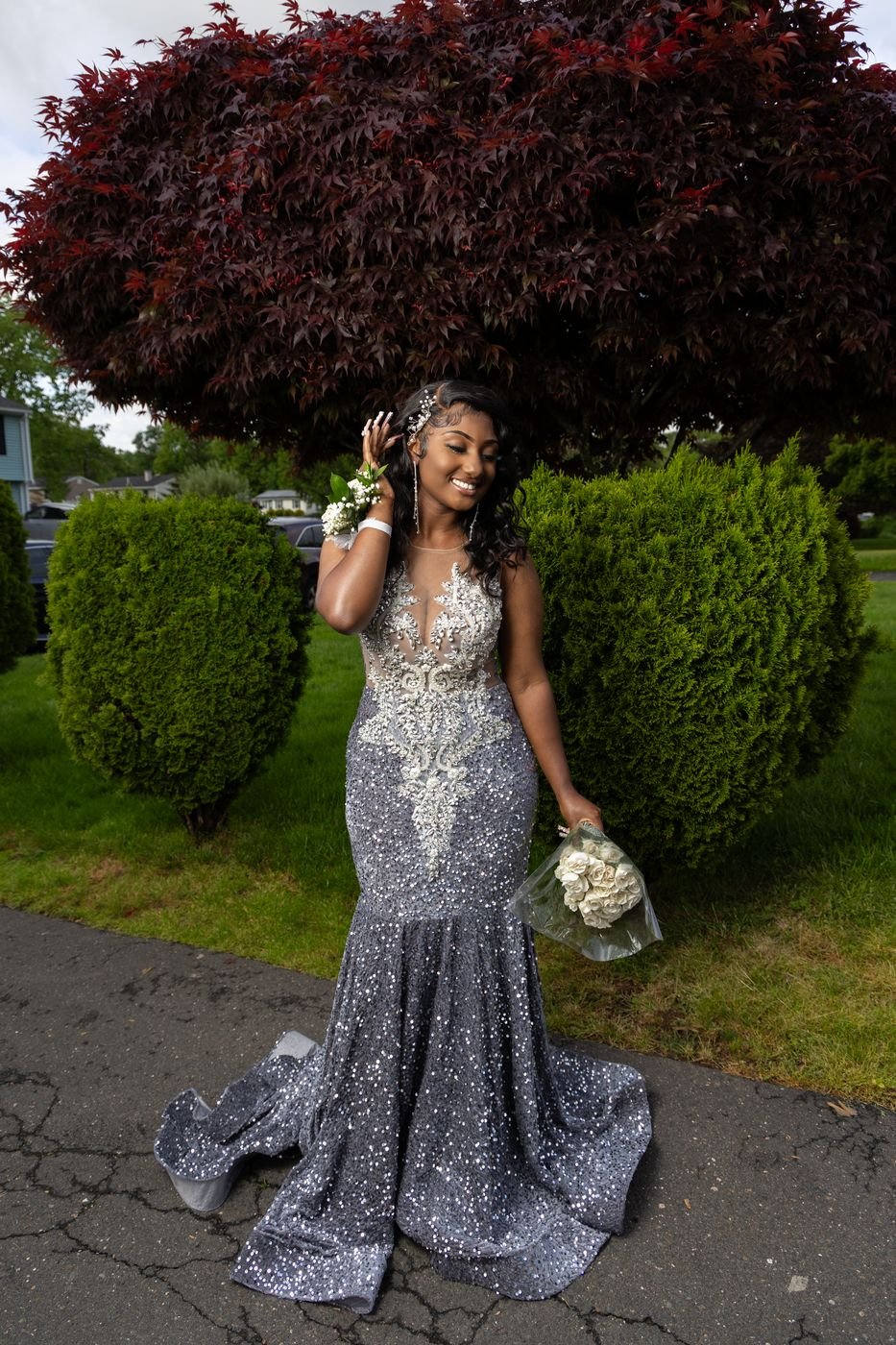 Woman in a sequin mermaid gown holding a bouquet under a red maple