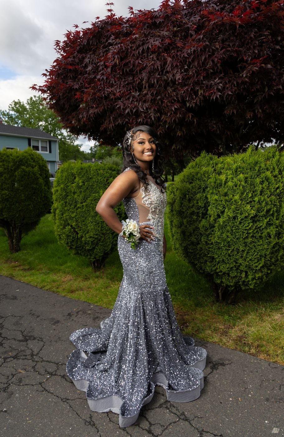 Woman in a silver sequin mermaid gown posing between garden shrubs