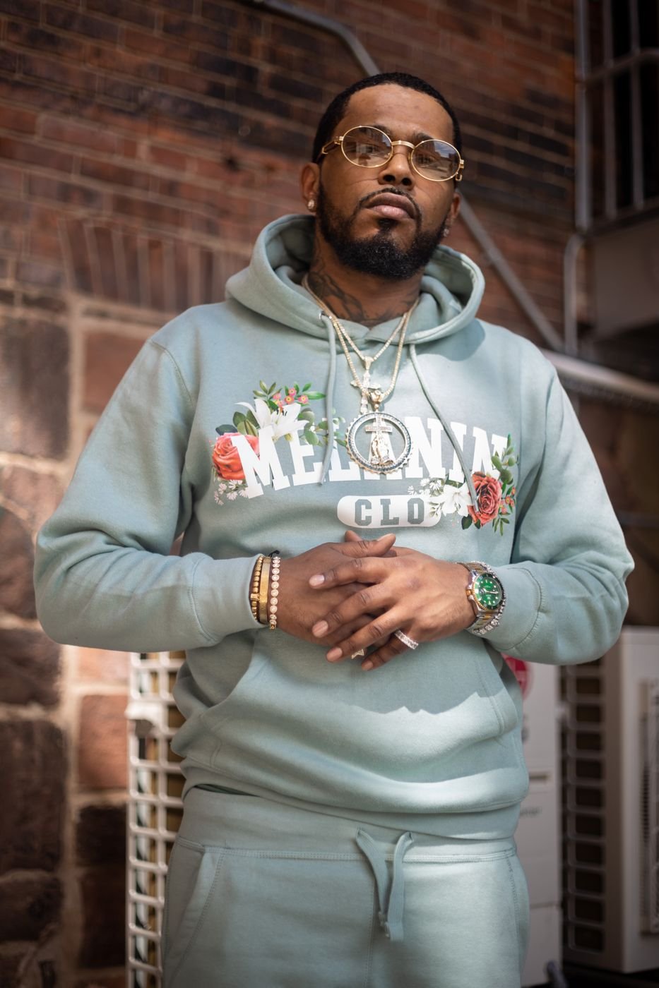 Model in a sage Melanin CLO floral hoodie against a brick wall